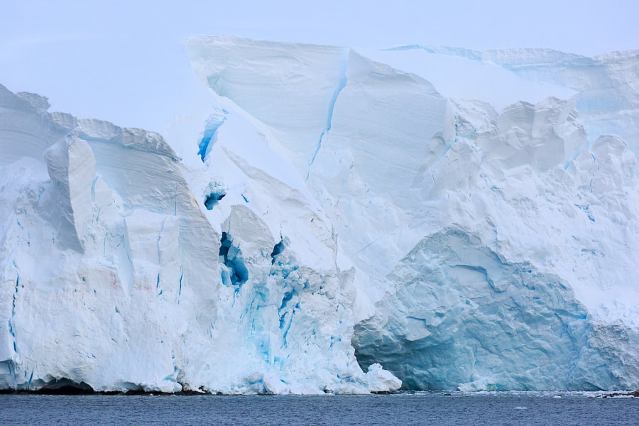 Sheer blue-white ice cliff of a tabular iceberg meeting the sea